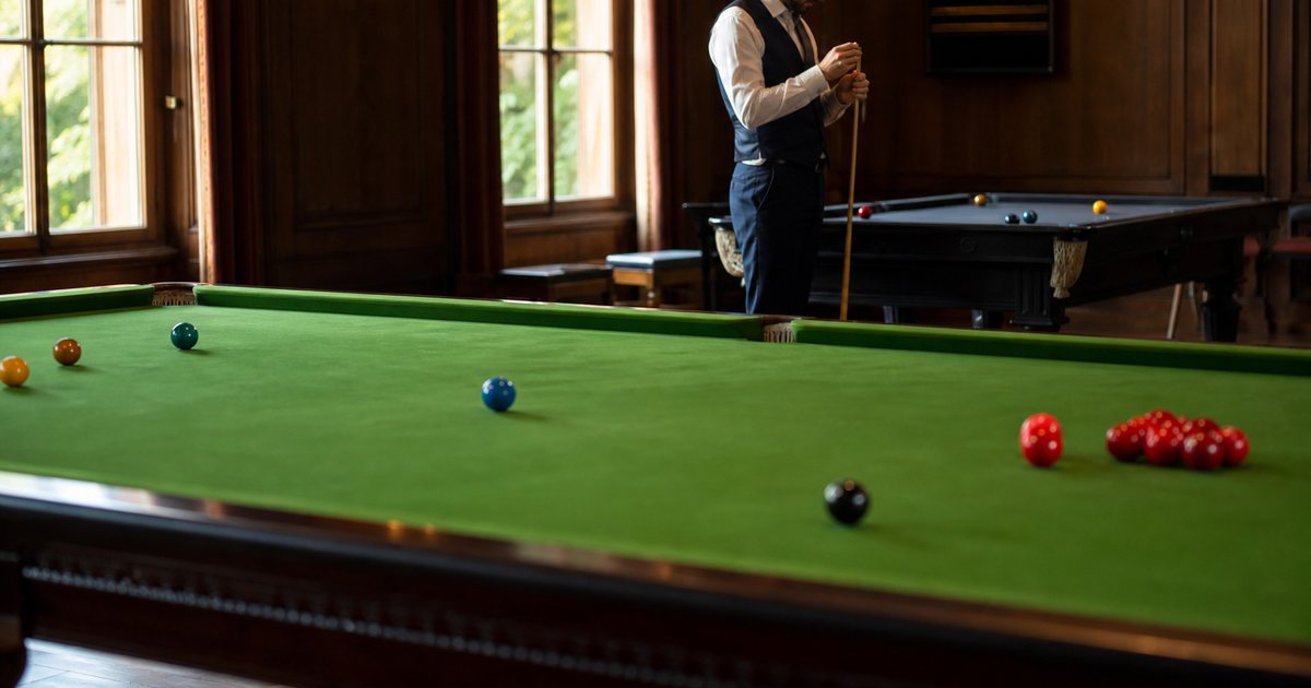 A grand wood-paneled billiard room with a very long green-cloth snooker table in the foreground and a smaller pool table beyond it, a man in a waistcoat chalking a cue beside the far table, tall windows letting in afternoon light